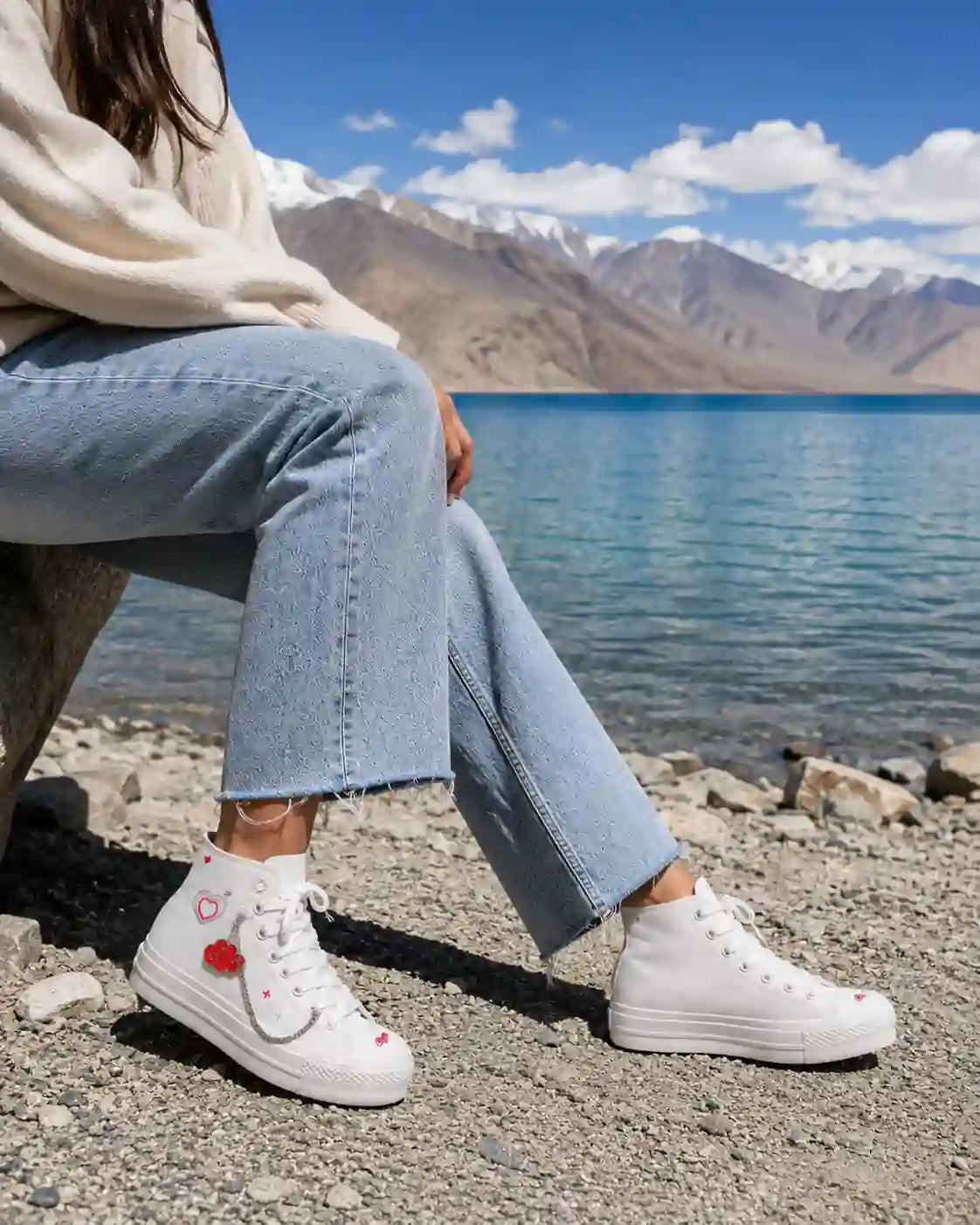 White high-top sneakers with Floating Feelings Edit red cloud shoe charm and silver chain beside a mountain lake