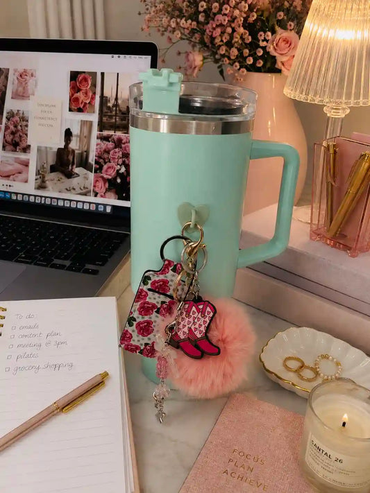Heartbreaker Boots Rubber Charm attached to a mint green tumbler with a fluffy pink pom pom and floral accessories