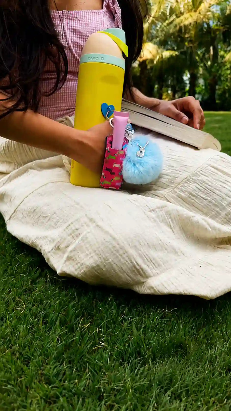 Woman sitting outdoors with a yellow water bottle decorated with the Butterfly Melody Water Bottle Charm while reading a book