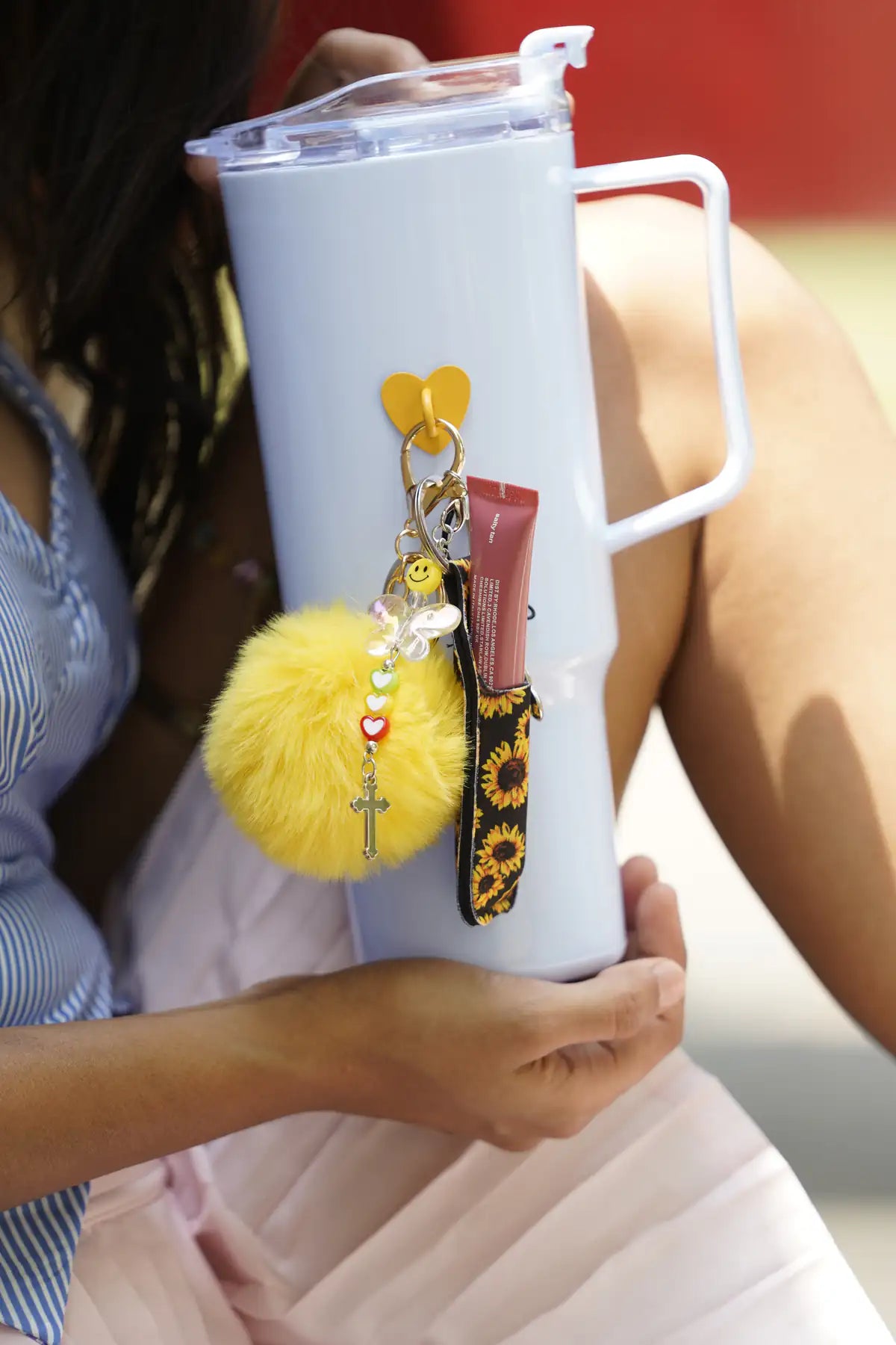 Butterfly Smile Water Bottle Charm attached to a light blue water bottle with a yellow pom pom and sunflower-patterned accessory