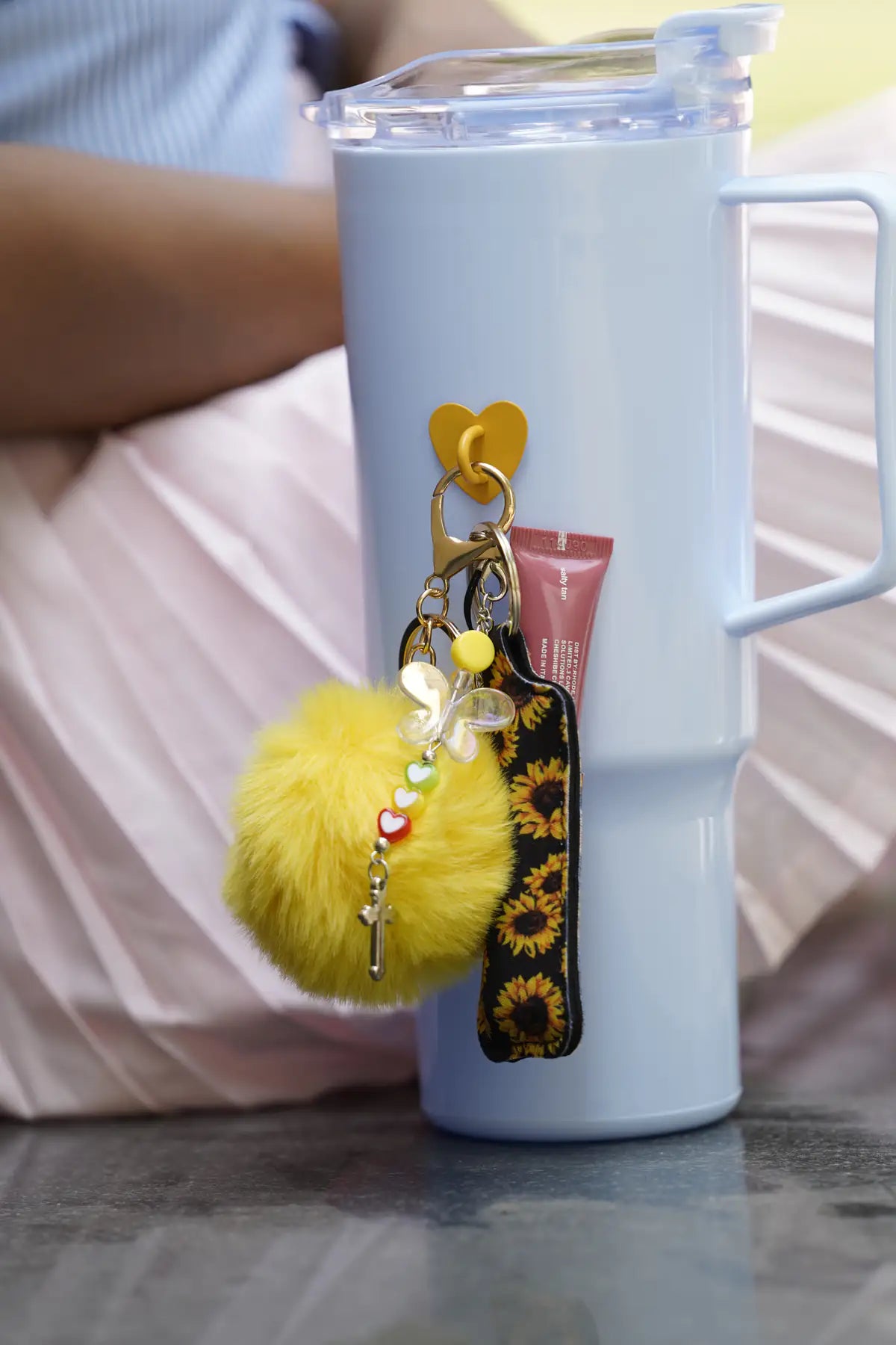 Close-up lifestyle view of the Butterfly Smile Water Bottle Charm attached to a light blue water bottle with a yellow pom pom and sunflower accessory