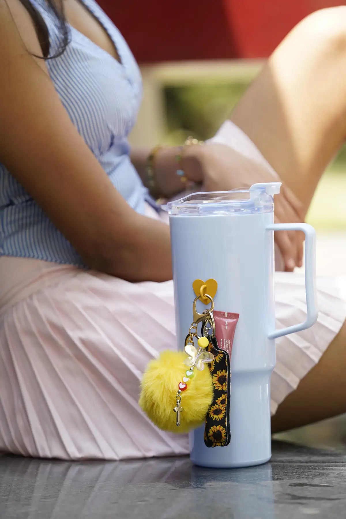 Light blue water bottle with Butterfly Smile Water Bottle Charm displayed beside a seated woman outdoors