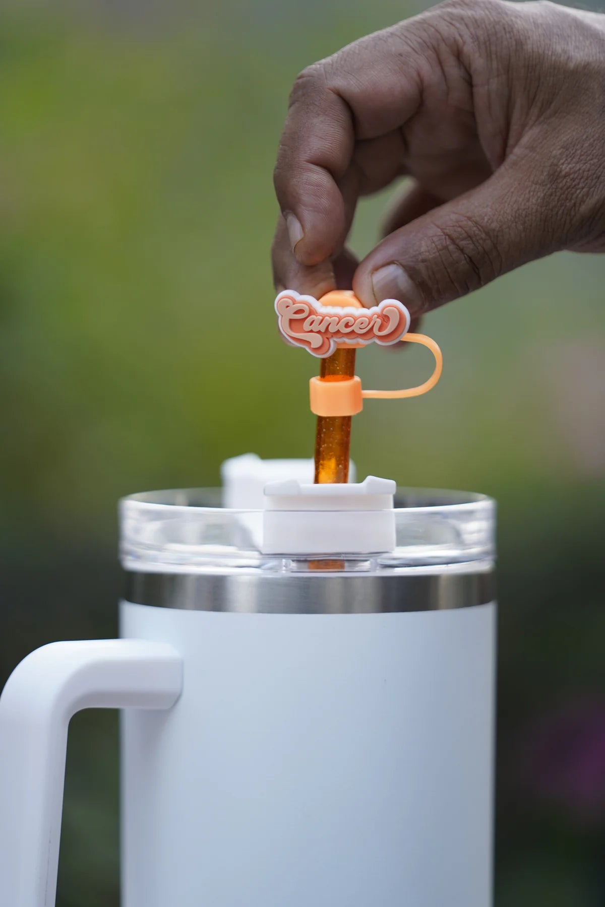 Hand attaching a Cancer zodiac straw charm to a glittery orange straw in a white tumbler