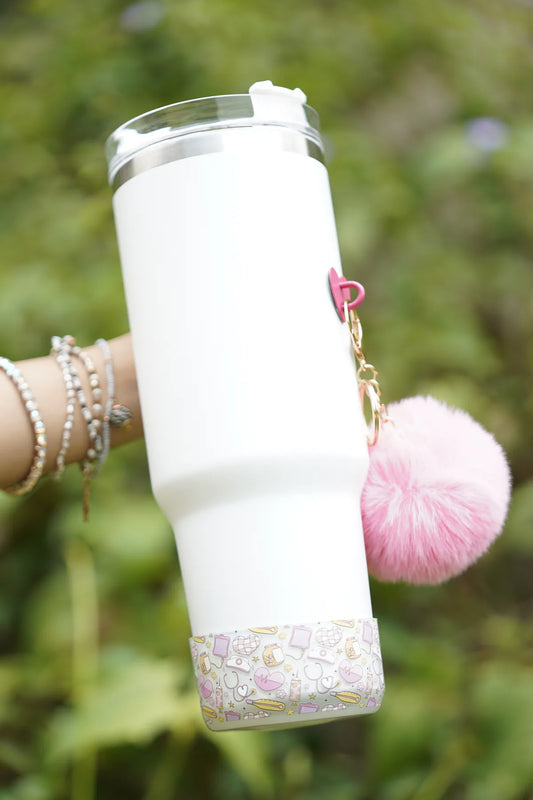 Nurse Chic water bottle boot fitted around the base of a white water bottle, featuring a pastel medical-themed pattern and a fluffy pink charm, shown outdoors.
