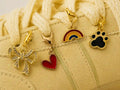 Close-up of the Rainbow State Edit gold bow, red heart, rainbow and black paw print shoe charms on a cream sneaker