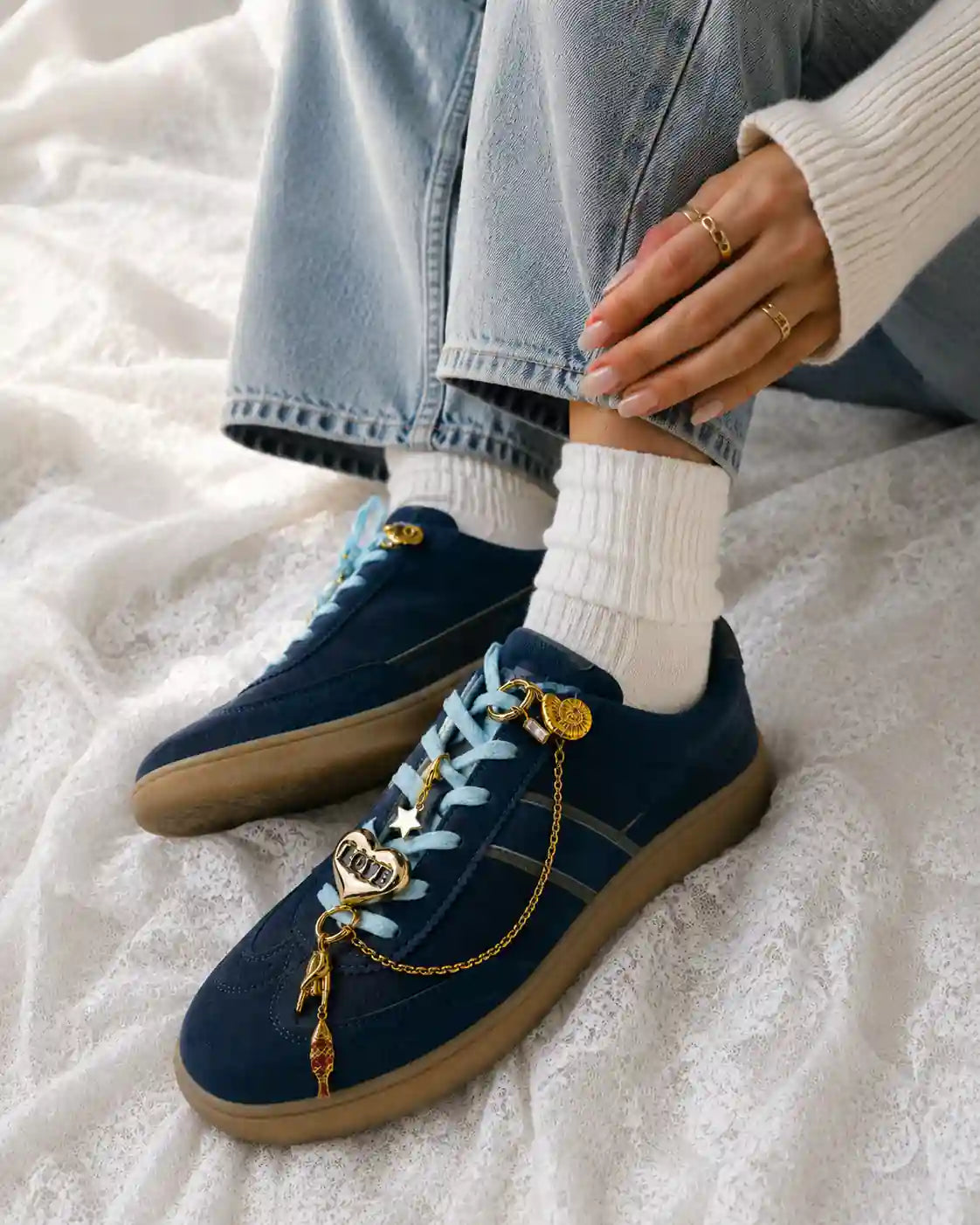 Person wearing navy sneakers styled with the Secret Crush Edit gold fish chain, LOVE heart and white star shoe charms