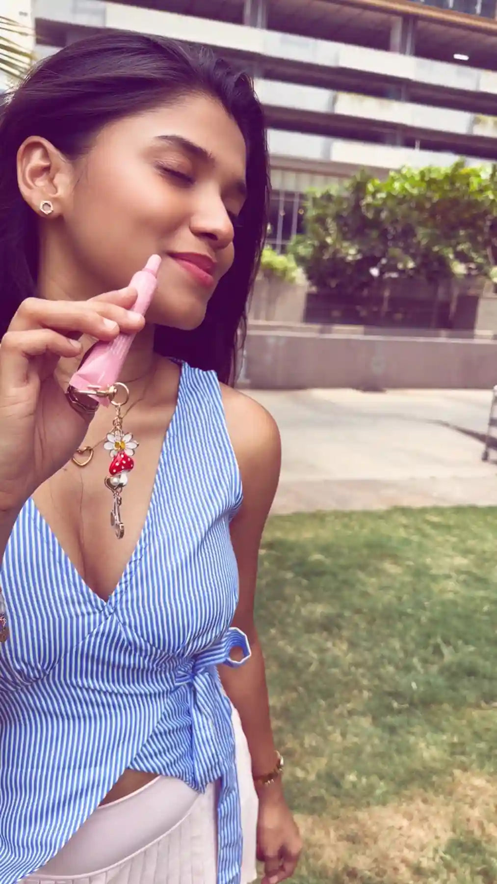 Woman using a pink lip balm with the cherry daisy charm attached