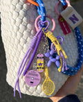 Lavender Rush Balloon Dog Bag Charm styled on a white woven bag with purple balloon dog, skateboard and tennis racket charms