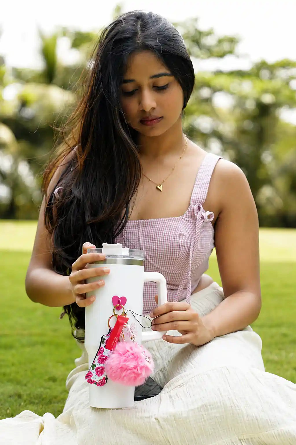 Peace Bow Water Bottle Charm attached to a white water bottle held by a woman outdoors, with a pink pom pom and floral accessory