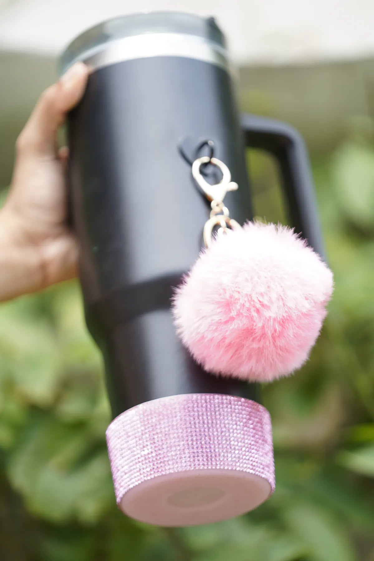 Pink bling water bottle boot attached to the bottom of a dark water bottle, with a fluffy pink charm hanging nearby.