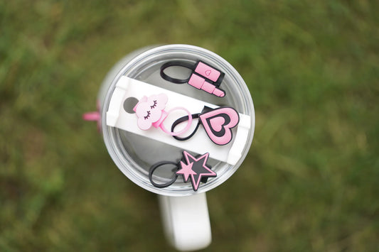 Four pink and black straw charms arranged on a white tumbler lid