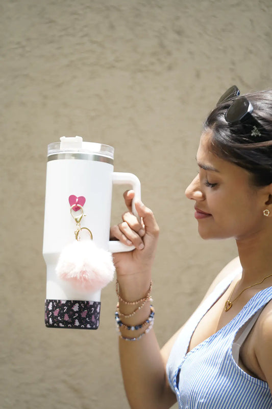 Pink holiday patterned water bottle boot fitted around the base of a white handled water bottle, shown being held outdoors.