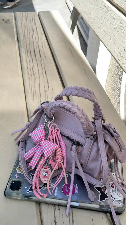 Pink gingham bow and layered cord bag charm attached to a lilac mini handbag