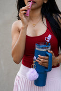 Woman holding a blue reusable water bottle with purple pom pom charm and bunny straw accessory