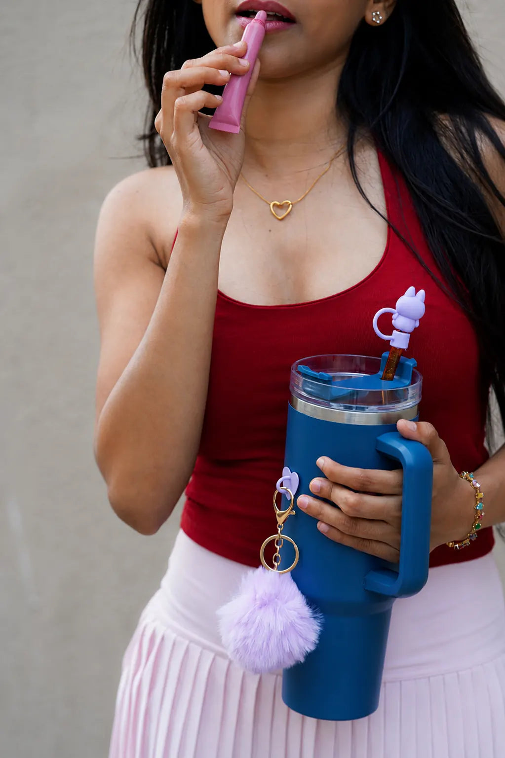 Woman holding a blue reusable water bottle with purple pom pom charm and bunny straw accessory