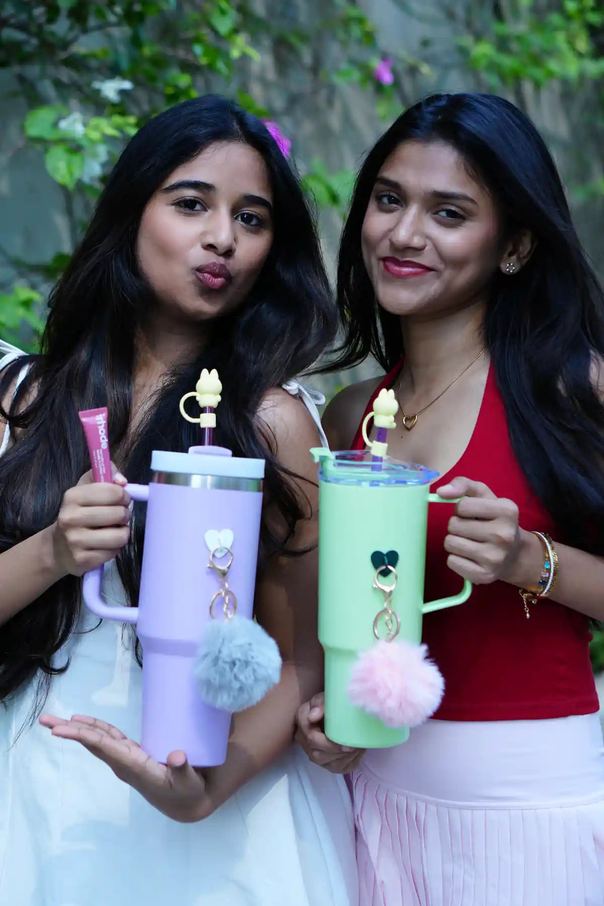 Two women holding pastel purple and green reusable bottles with pom pom charms and bunny straw accessories
