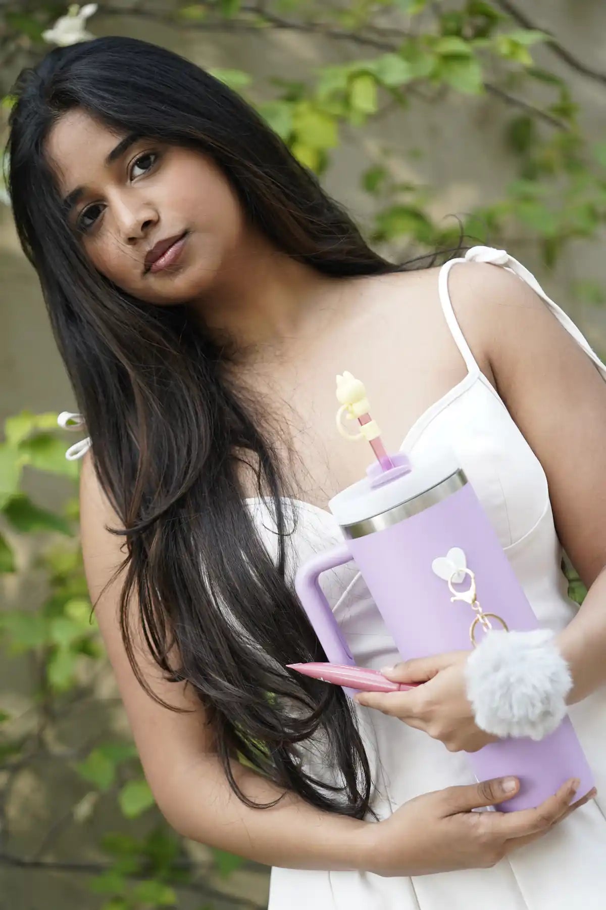 Woman holding a pastel purple reusable bottle with grey pom pom charm and yellow bunny straw accessory
