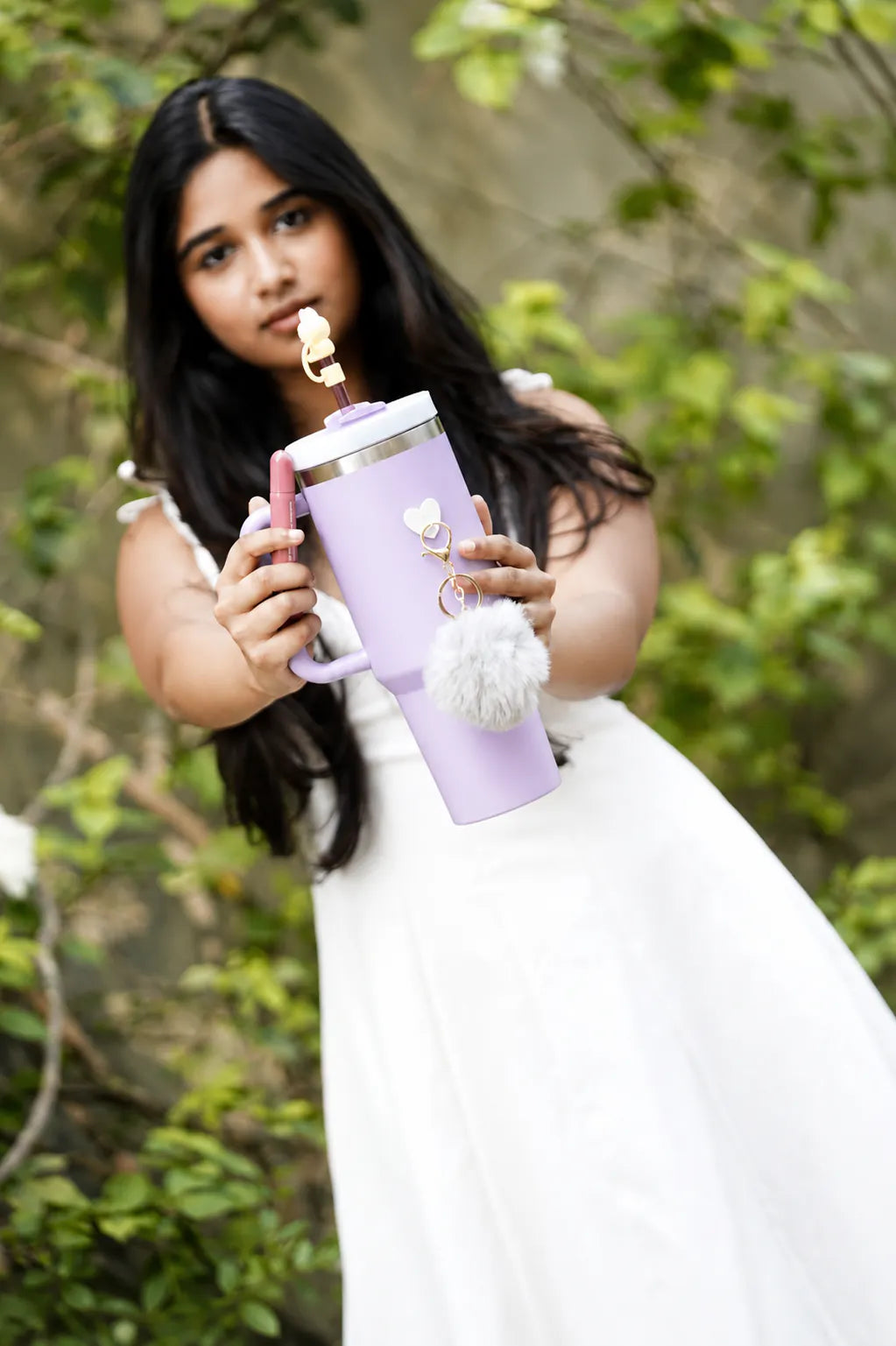 Woman holding a pastel purple reusable bottle with grey pom pom charm and yellow bunny straw accessory
