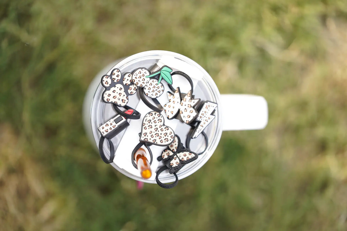 Seven leopard print straw charms arranged on a tumbler lid outdoors